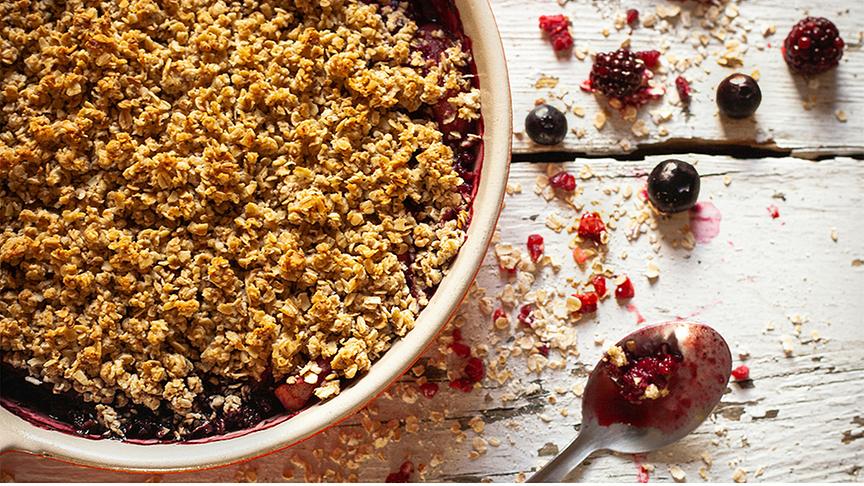 Heidelbeercrumble in einer Schale, daneben ein Löffel und Krümel des Crumble sowie einige Beeren.