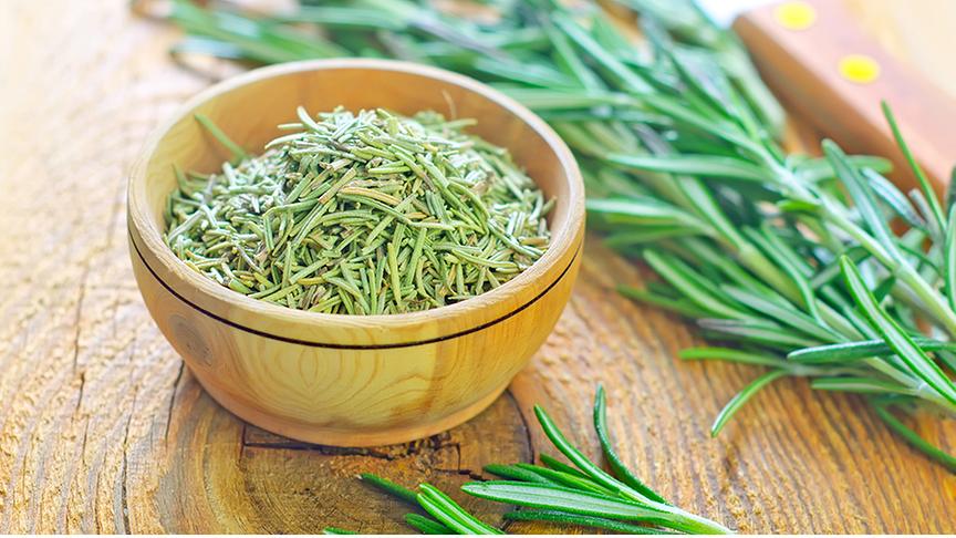 Eine kleine Holzschale gefüllt mit getrockneten Rosmarinblättern, daneben ein frischer Rosmarinstängel