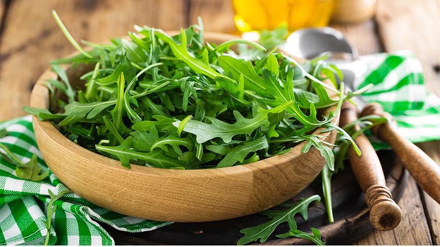 Holzschale gefüllt mit Rucola auf einer Stoffserviette neben Besteck.