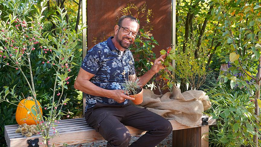 Karl Ploberger auf einer Sitzbank mit herbstlicher Deko.