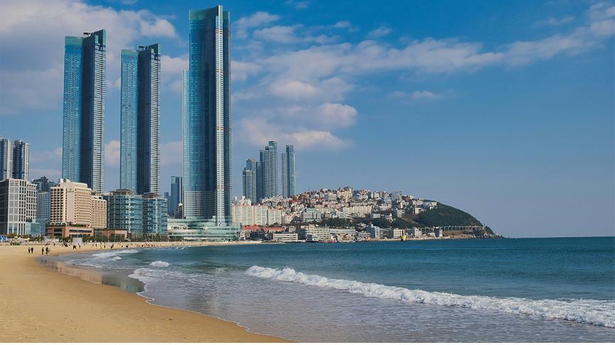 © Foto: Unsplash Strand mit Meer und hohen Hochhäusern sowie anderen Gebäuden im Hintergrund.