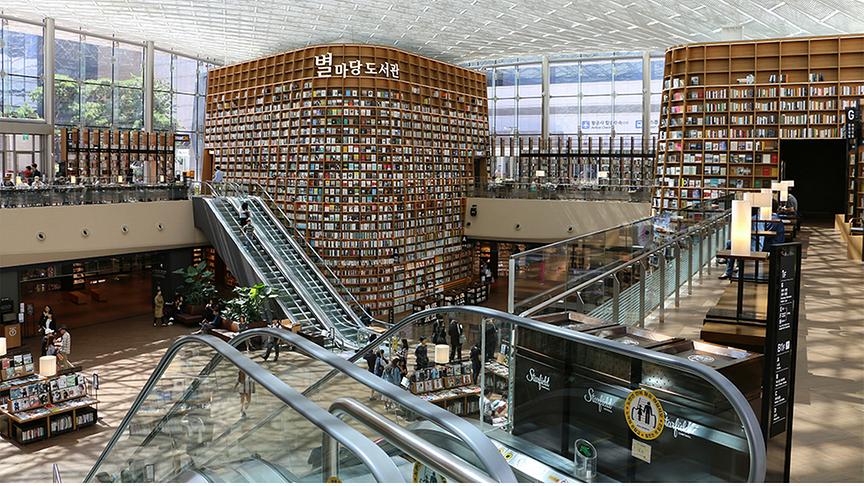 © Foto: Unsplash Bibliothek über zwei Etagen, die mit Rolltreppen verbunden sind, mit meterhohen Regalen und moderner Architektur.