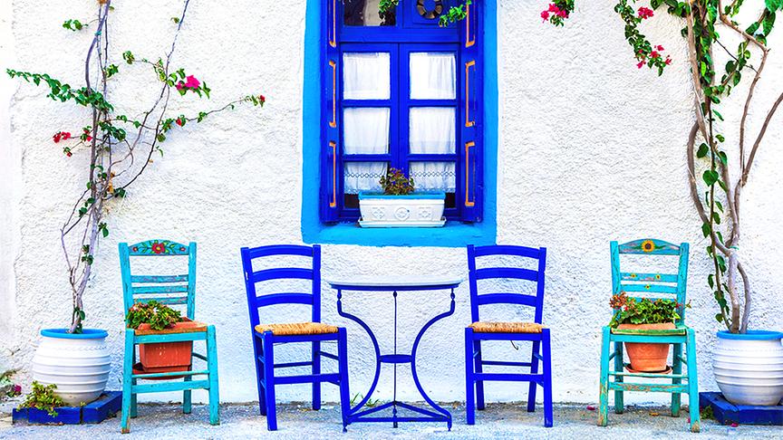 Blaue Stühle vor einer weißen im typischen Griechenland-Design