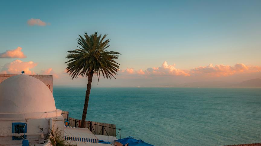 Weiße Häuser mit blauen Türen und Fenstern an einer Küste mit Blick auf das Mittelmeer.