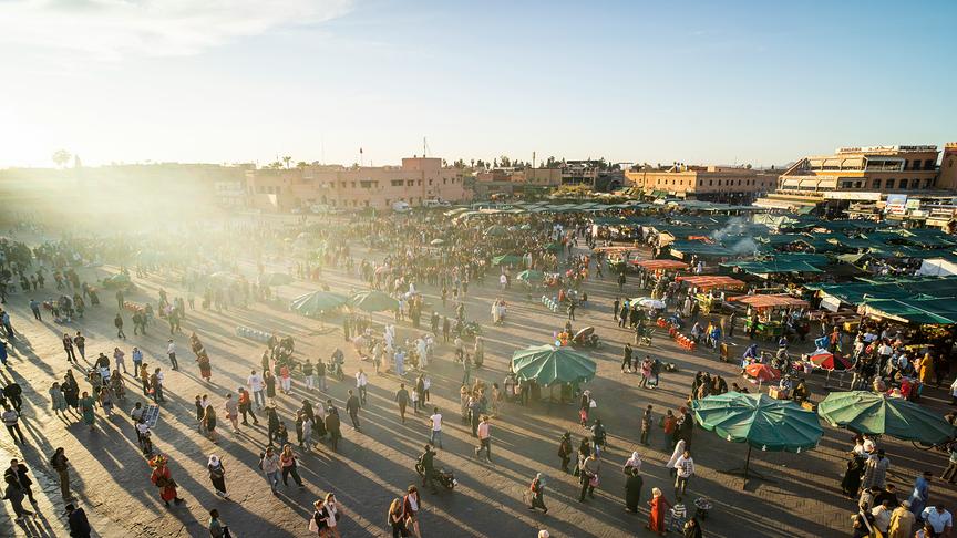 Großer Platz mit Menschen, Marktständen und historischen Gebäuden bei Sonnenuntergang.