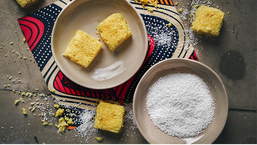 Kashata za nazi - Dicke Kokosplätzchen - zwei Schüsseln, eine mit den Kokosplätzchen, die andere mit Kokosraspeln auf einem afrikanisch aussehenden Untersetzer.