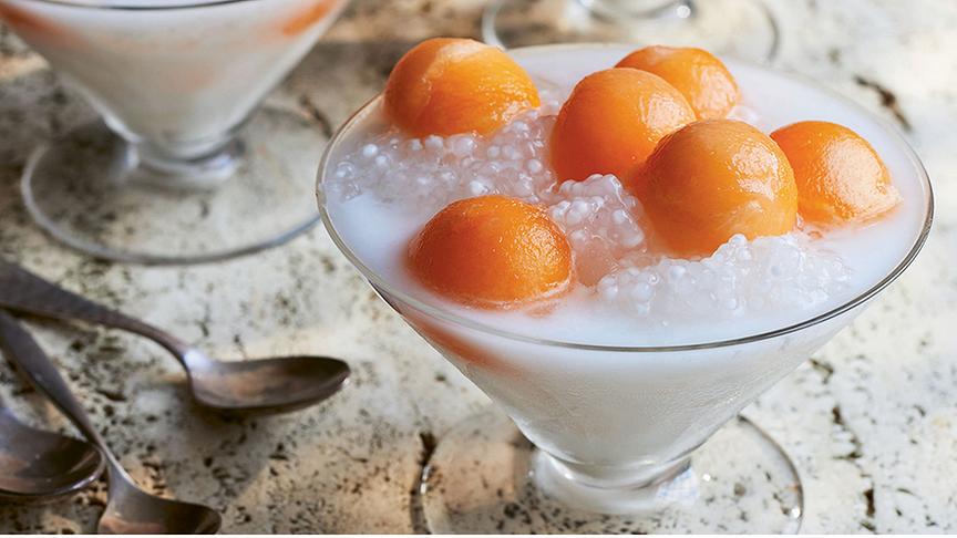 Melonenkugeln mit Sago in Kokossirup in kegelförmigen Dessertgläsern. Die orangen Melonenkugeln liegen auf einer weißen Menge aus Sagoperlen und Kokossirup. 