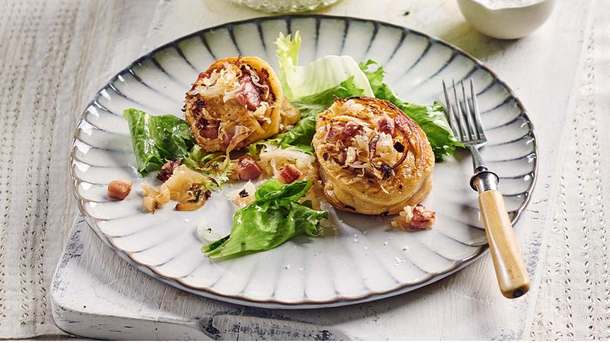 Ein Teller auf dem zwei Krautkrapfen mit Salat und einer Gabel schön angerichtet sind.