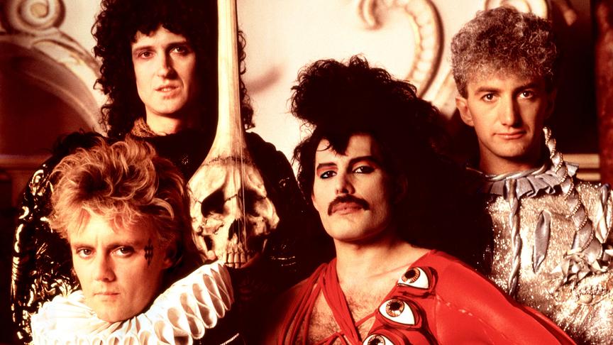 Foto der vier Queen-Mitglieder in ausgefallener Kleidung und mit einem Totenkopf-Schädel zwischen ihnen herunterhängend.