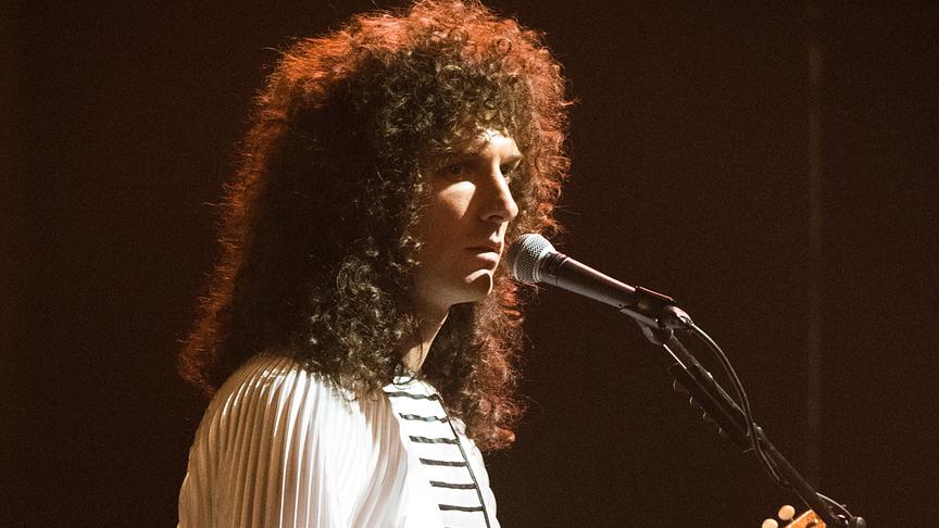 Mann mit langen Locken steht vor einem Mikrofon