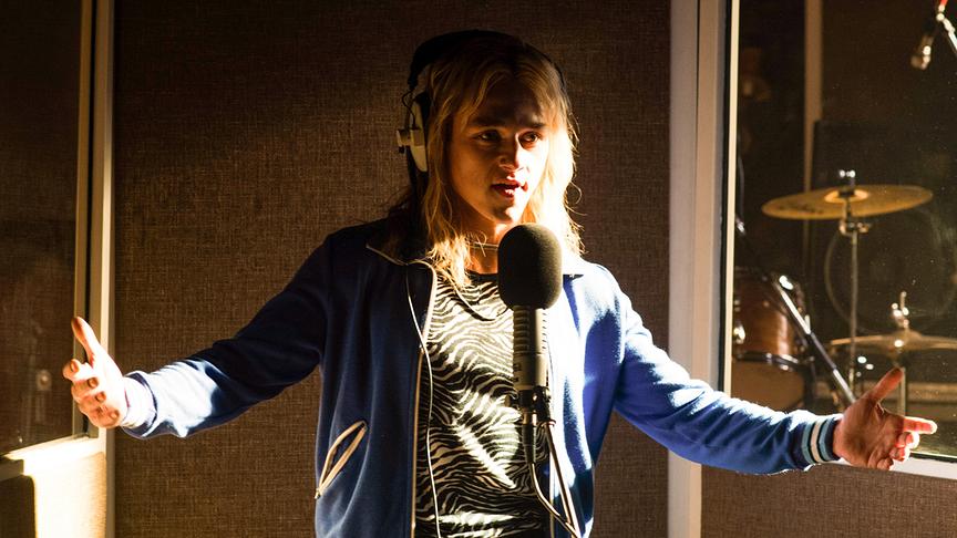 Mann steht mit ausgebreiteten Armen und Kopfhörern vor dem Mikrofon in einem Tonstudio