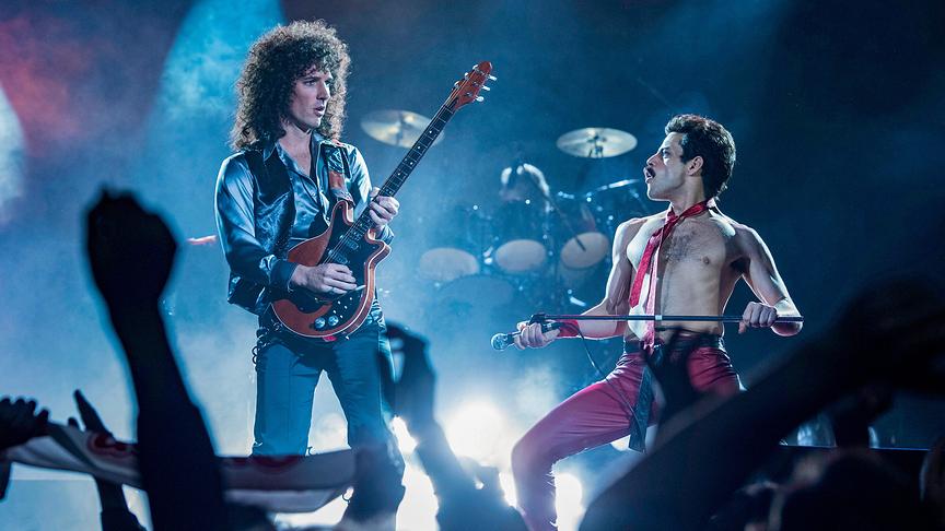 Zwei Männer, einer mit Gitarre und einer mit Mikrofon, performen auf einer Bühne vor Publikum