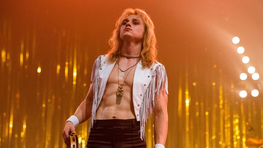 Mann mit langen, blonden Haaren in offener Fransenweste