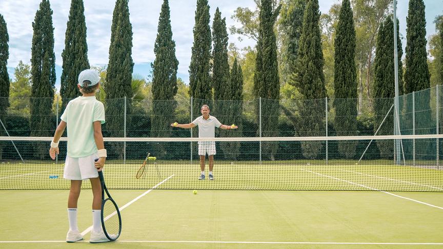 © Foto: ORF/ProSieben/LEONINE Studios Ein Mann und ein Junge stehen sich im Tennisoutfit auf einem begrünten Tennisplatz gegenüber. Das Netz ist zwischen ihnen, der Vater hat beide Hände erhoben und hält in jeder Hand einen Tennisplatz. Der Junge steht bereit mit Tennisschläger in der Hand gegenüber.