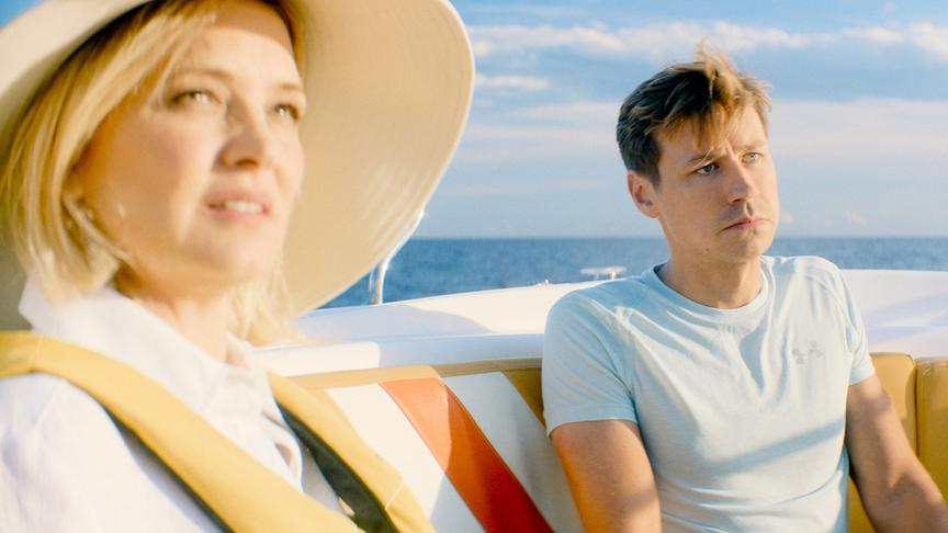 © Foto: ORF/ProSieben/LEONINE Studios Ein Mann im T-shirt und eine Frau mit Sonnenhut auf einem Boot im Meer bei Sonnenschein nebeneinander sitzend.