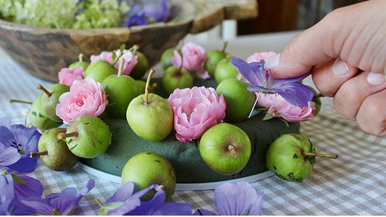 Steckring mit einigen Blüten und kleinen Äpfeln. Eine Hand stecke gerade eine weitere Blüte hinein.