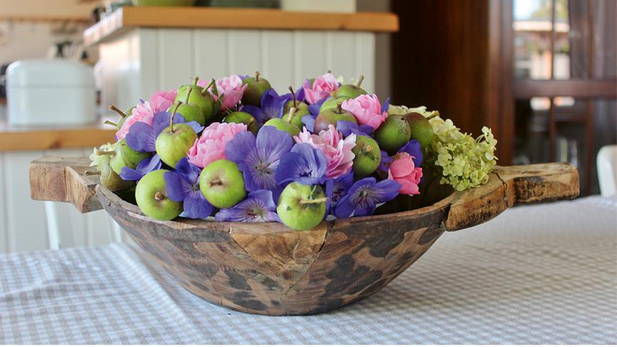 Holzschale mit verschiedenen Blüten und kleinen Äpfeln.