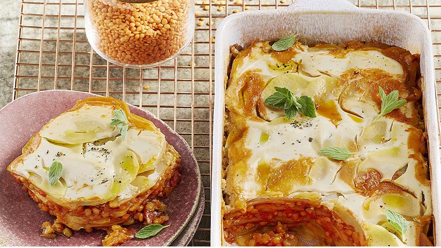 © © Katrin Winner Ofenform und Schüssel mit Kartoffel Lasagne sowie ein Glas mit orangen Linsen
