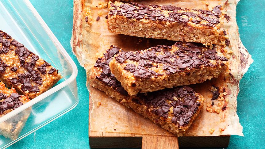 Mehrere Quinoa Crumble Bars liegen nebeneinander auf einem Küchenbrett. Daneben sieht man auch ein paar Riegel in einer Vorratsbox.