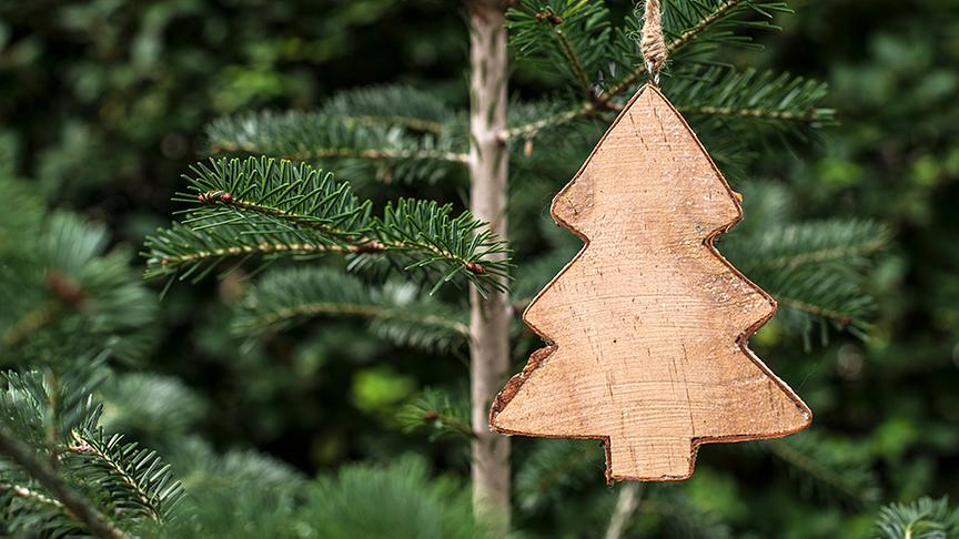 Christbaum aus Holz hängt an einem Tannenzweig