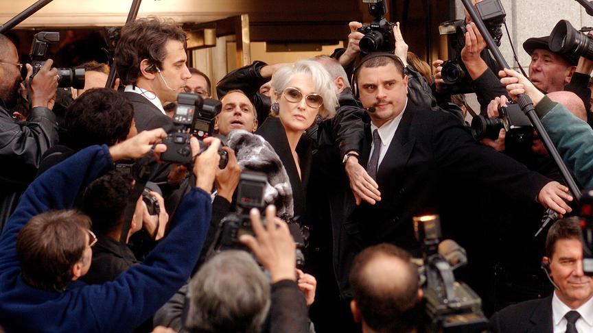 Frau umgeben von Bodyguards und Fotografen