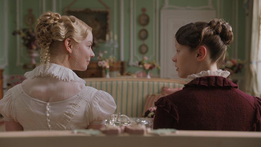 Zwei Frauen sitzen nebeneinander auf einem Sofa und blicken sich an.