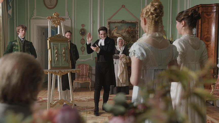 Raum voller Personen, in der Mitte ein Stativ mit einem Kunstobjekt, das gerade von einem Mann vorgestellt zu werden scheint.