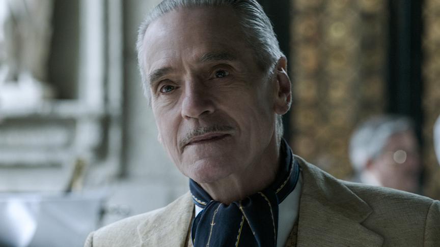 Ein Mann mit grauen Haaren und Schnauzbart, in einem edel wirkendem Raum