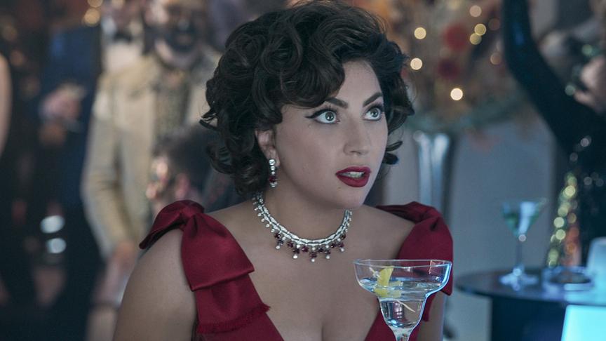 Eine Frau mit dunklen Locken und einem roten Abendkleid, im Hintergrund weitere Personen