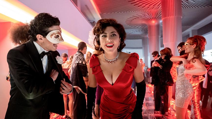 Im Vordergrund: Ein Mann und eine Frau in Abendgarderobe, der Mann trägt eine Maske; im Hintergrund: weitere Personen in Abendgarderobe und Maskierung