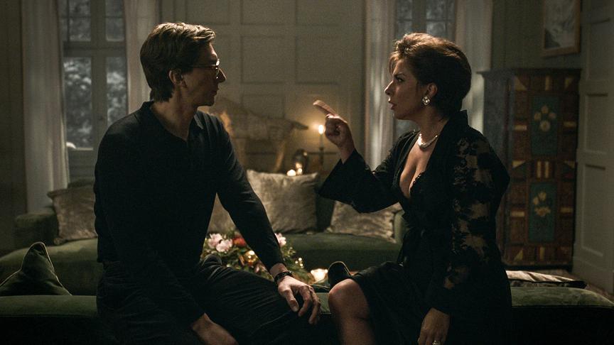 Eine Frau mit erhobenem Zeigefinger sitzt auf einer Couchlehne einem Mann gegenüber und blickt ihn eindringlich an.