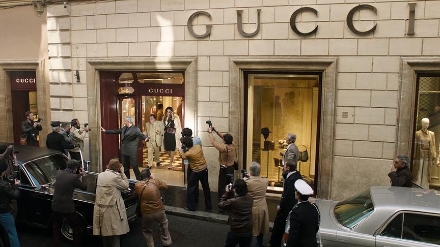 Vor einem Gucci-Geschäft steht eine Gruppe von Fotografen, die Personen, die gerade aus dem Geschäft herauskommen, fotografieren.