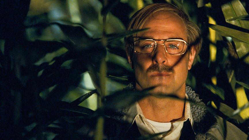 Mann halb verborgen hinter einer Pflanze.