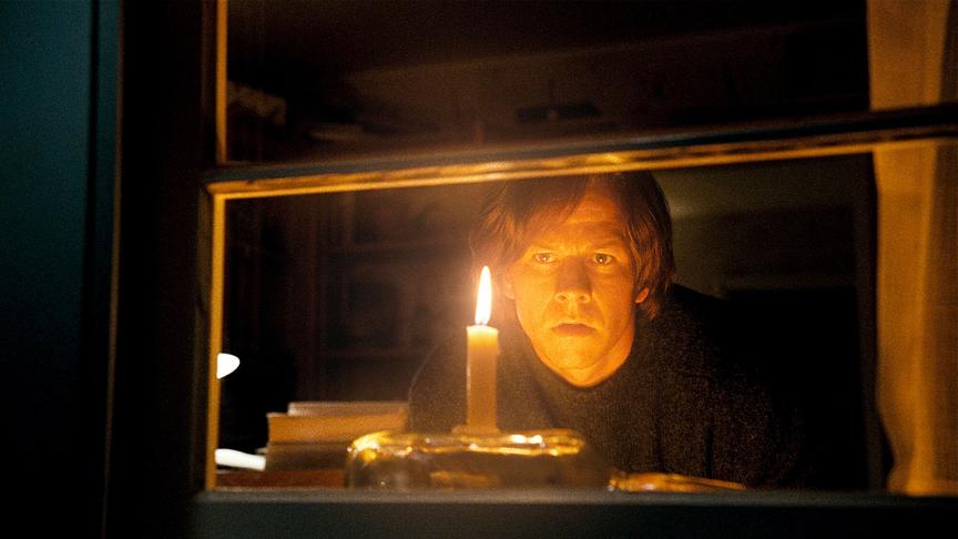 Mann blickt an einer erleuchteten Kerze vorbei durch ein Fenster.