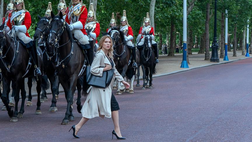 Eine Frau mit hohen Schuhen geht direkt vor der britischen Reitergarde über eine Straße.