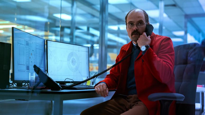 Ein Mann telefoniert mit Hörer am Ohr an einem Schreibtisch mit moderner Ausstattung.