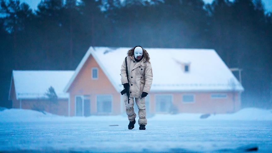 Ein Mann in Schneebekleidung und mit Waffe in eisiger Umgebung, sein Gesicht ist von einer weißen Maske und Blut bedeckt.