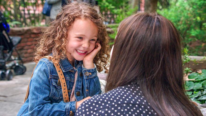 Ein kleines Mädchen lächelt eine ihr gegenüber kniende Frau an.