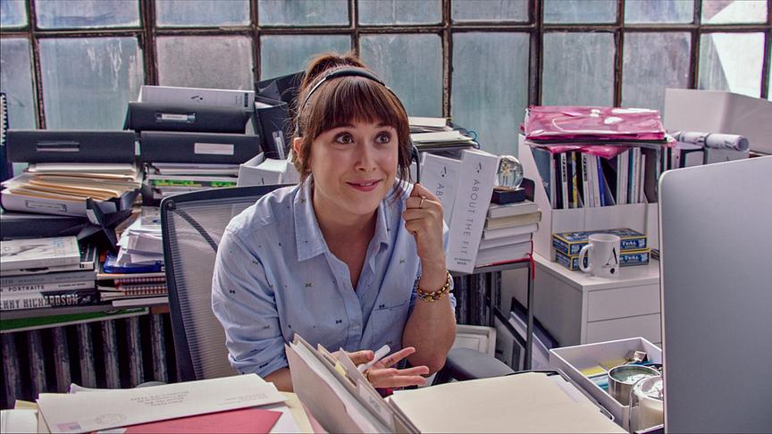 Eine Frau mit Headset an einem mit Akten vollen Schreibtisch