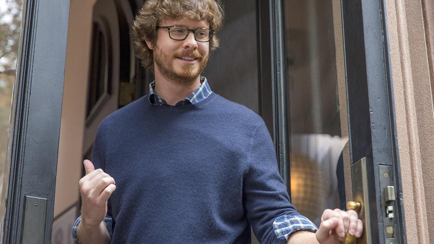 Ein Mann steht in einer Tür und zeigt mit seinem Daumen nach drinnen.