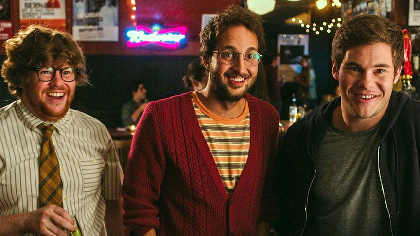 Drei Männer stehen lachend nebeneinander in einer Bar