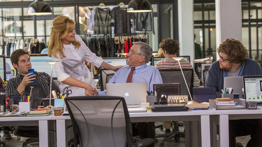 Mehrere Personen in einem Büro, eine Frau schüttelt die Hand eines sitzenden Mannes