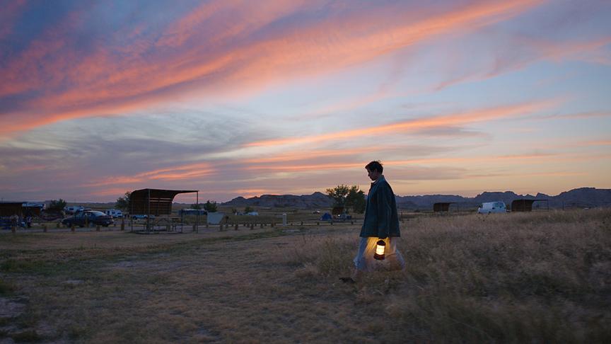 Frau mit Laterne läuft über eine Grasebene bei Dämmerung.