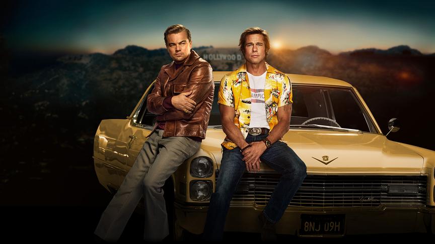 Zwei Männer sitzen auf der Motorhaube eines Autos, im Hintergrund der Hollywood-Schriftzug