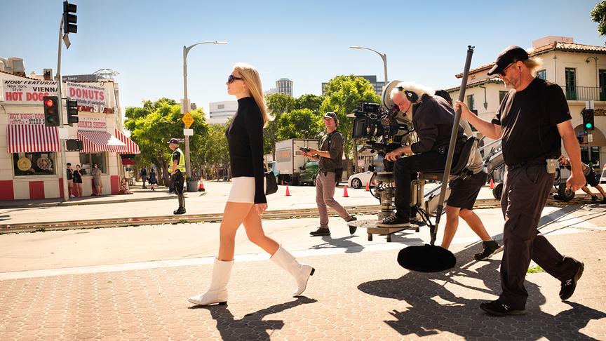 Eine Filmcrew filmt eine Frau durch eine Straße gehen.