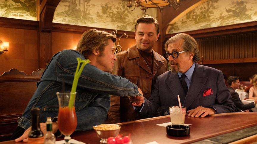 Drei Männer mit Drinks an einem Bartresen, zwei davon schütteln sich die Hände