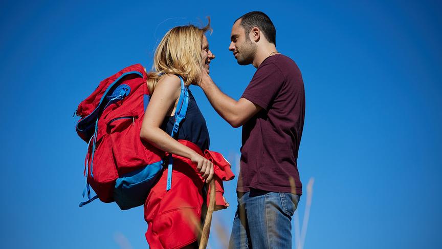 © Eine Frau mit Rucksack und ein Mann stehen sich gegenüber. Der Mann hält eine Hand an das Gesicht der Frau.