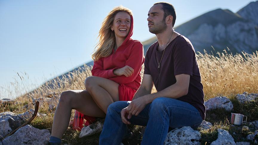 © Foto: ORF/Bravado Media/MarVista Entertainment/Umberto Poto Eine Frau und ein Mann sitzen auf Steinen in der Natur. Die Frau lächelt den Mann an.
