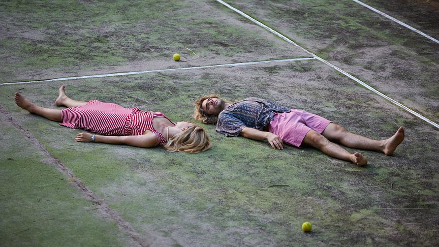 © Foto: ORF/Bravado Media/MarVista Entertainment/Umberto Poto Eine Frau und ein Mann liegen in unterschiedliche Richtungen, aber mit dem Gesicht auf gleicher Höhe nebeneinander auf einem Tennisfeld.