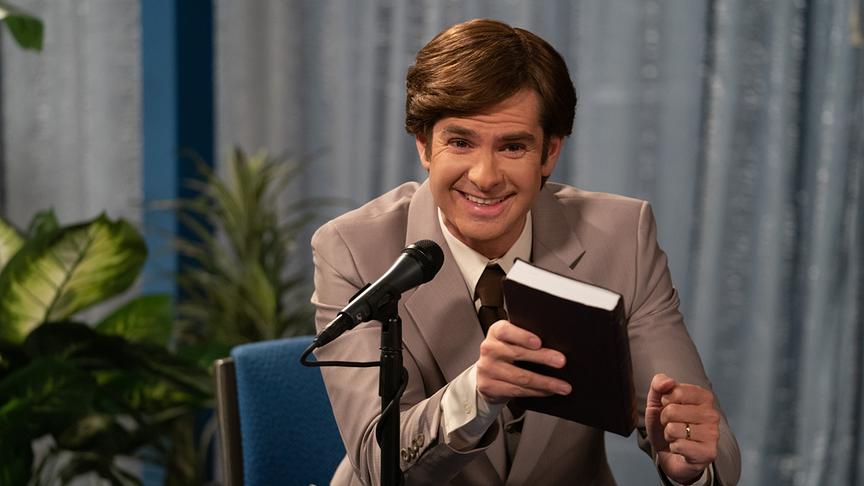 Ein Mann sitzt vor einem Mikrophon an einem Tisch und hält ein Buch in der Hand.